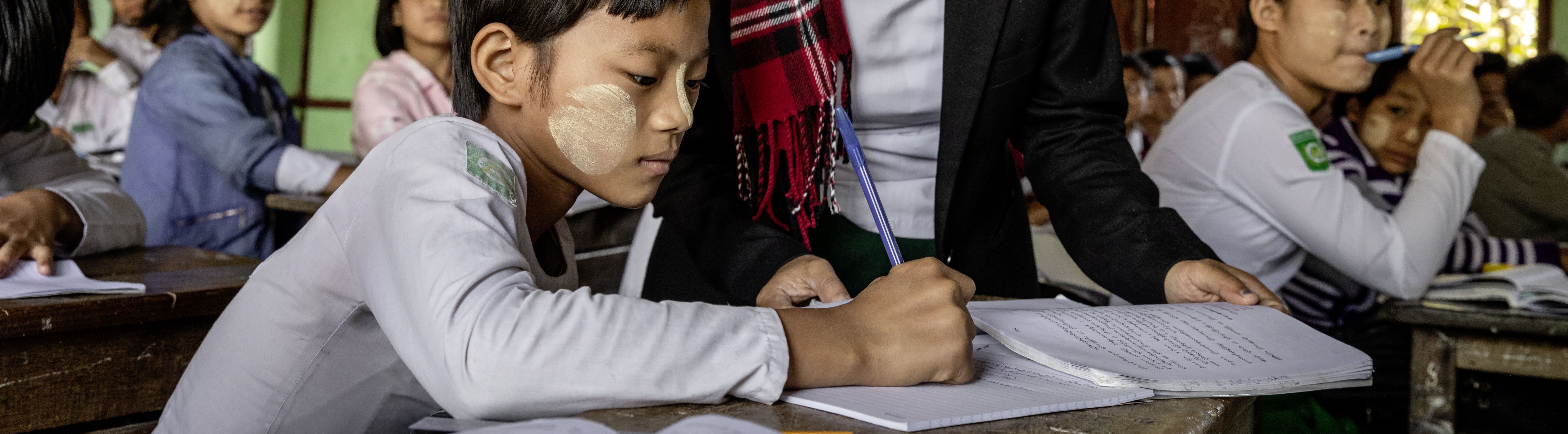 Lehrerin steht am Tisch eines Schülers und erklärt ihm etwas