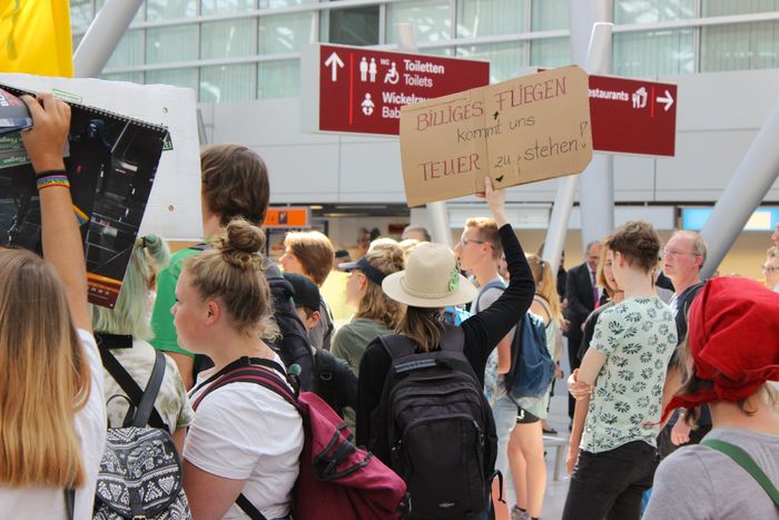 Schild der Protestierenden mit der Aufschrift: billiges Fliegen kommt uns teuer zu stehen 